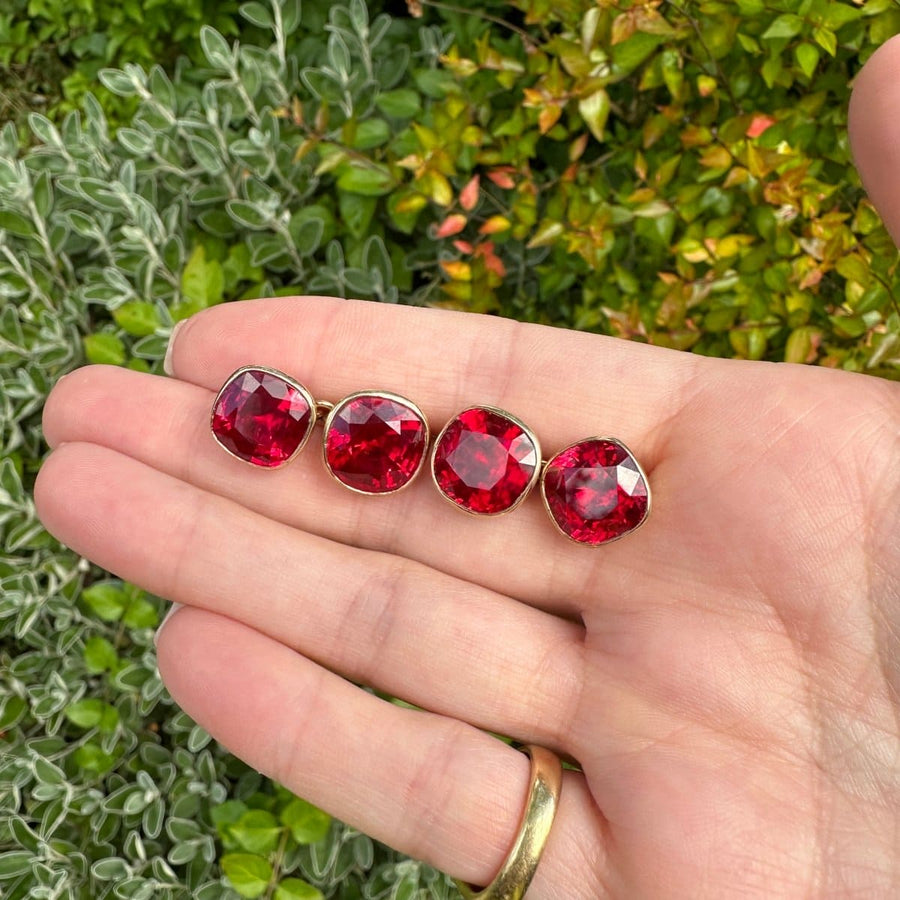 1940s 9ct gold red paste cufflinks displayed in hand against a green foliage background, showcasing vibrant red stones.