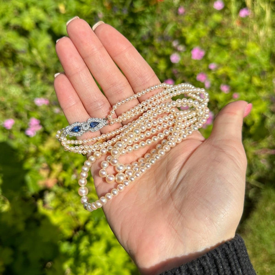 Dreistrangige Zuchtperlenkette aus den 1940er Jahren mit Saphir- und Diamantverschluss in der Hand, mit cremeweißen Perlen.