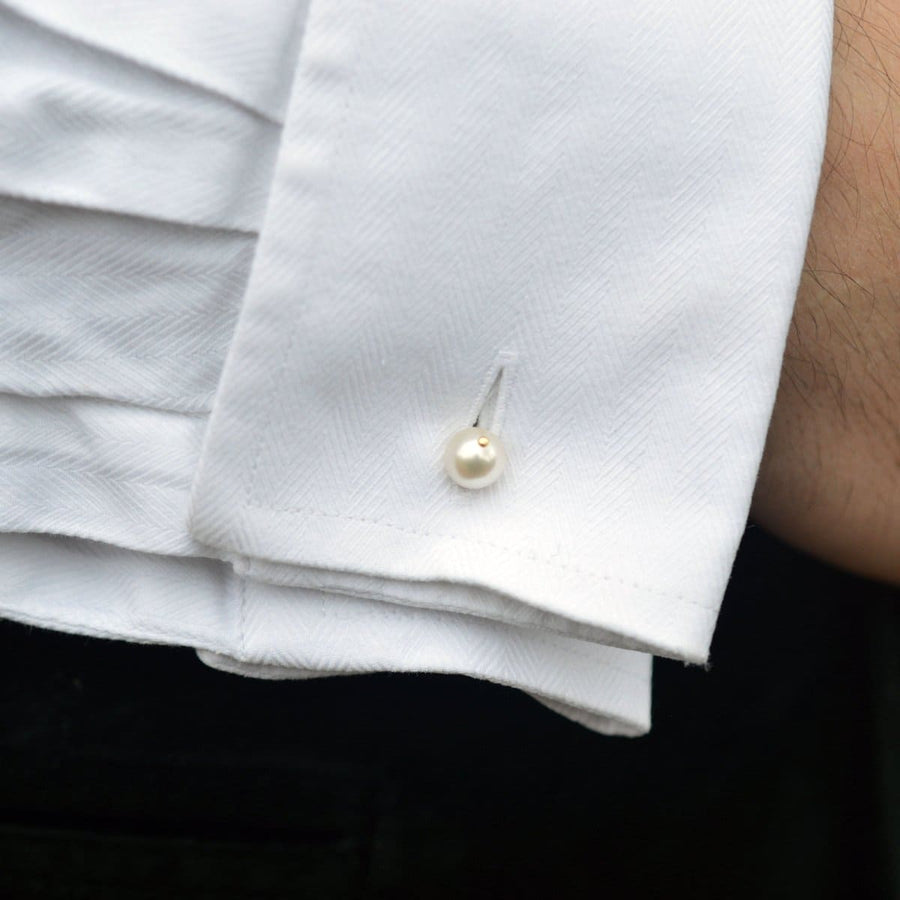 Nahaufnahme einer weißen Hemdmanschette mit einer einzelnen Zuchtperle, die den eleganten Stil eines Manschettenknopfes unterstreicht.