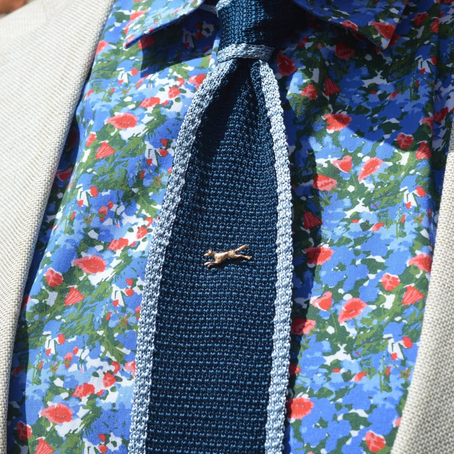 1950s 9ct gold running fox tie pin attached to a navy tie with a floral shirt background.