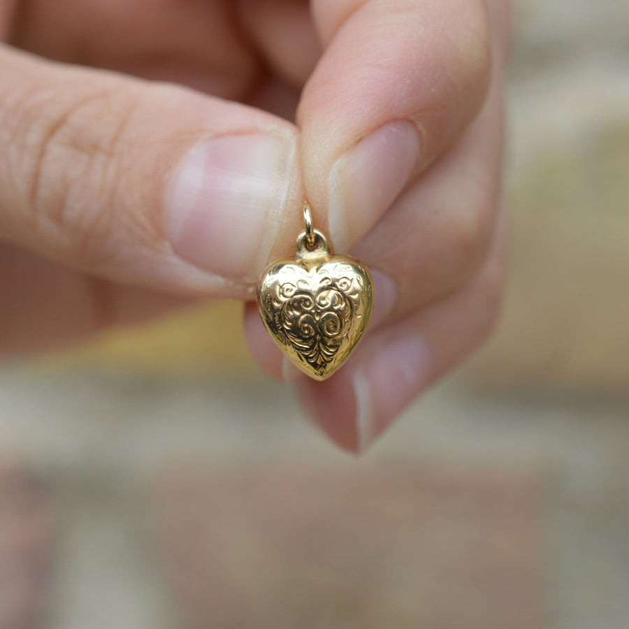 Small 1960s 9ct gold puffy heart pendant charm with scroll engravings, held by a hand.