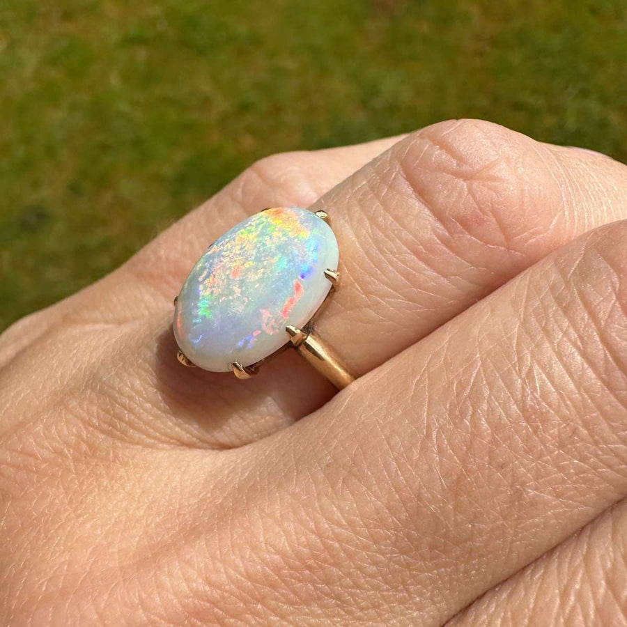 Art-Deco-Ring aus 18-karätigem Gold mit weißem Opal, der auf einer Hand lebhaft rot und bunt aufblitzt.