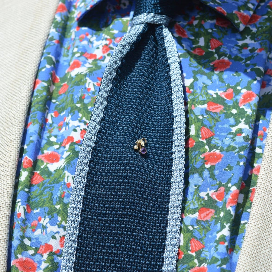 Art Deco 9ct gold tie pin with amethyst and pearl on a textured tie, surrounded by floral patterned shirt.
