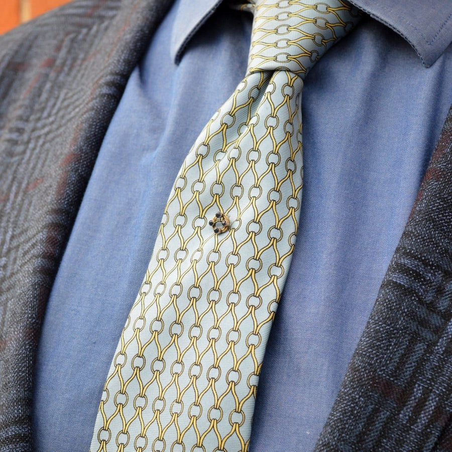 Art Deco 9ct gold tie pin with sapphires on a patterned silk tie, showcasing a timeless geometric design.