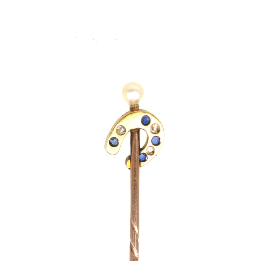 Edwardian gold horseshoe tie pin with sapphire, diamond accents, and natural pearl on top, dating to the 1900s.