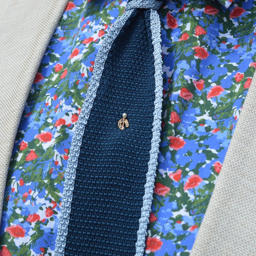 Close-up of a tie pin featuring a decorative design, worn on a patterned floral shirt with a beige blazer.