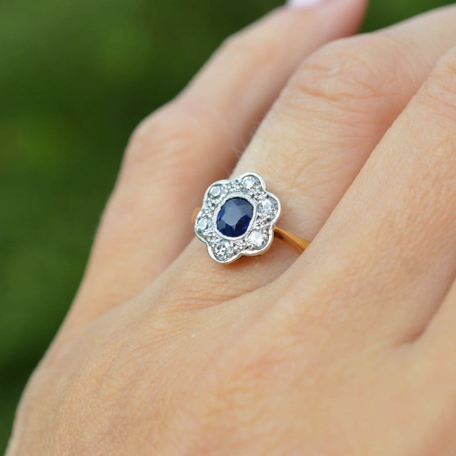 Edwardian 18ct gold and platinum sapphire diamond cluster ring on a hand, showcating elegance and brilliance.