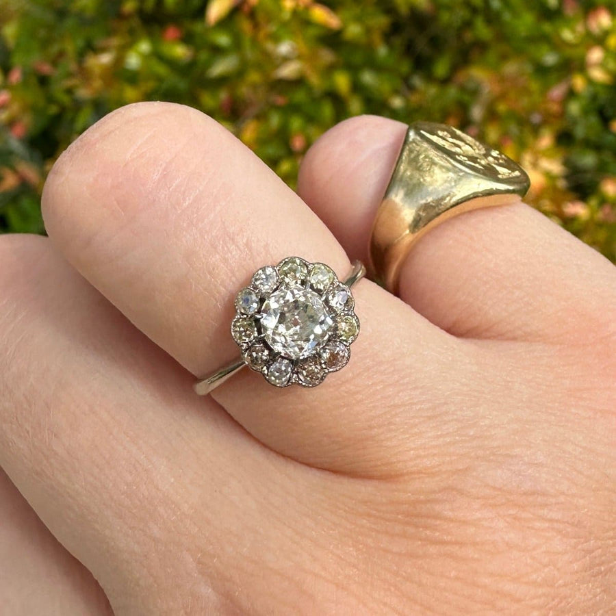 Edwardian 18ct white gold diamond cluster ring on a hand with a gold band, showcasing an old mine cut center diamond.