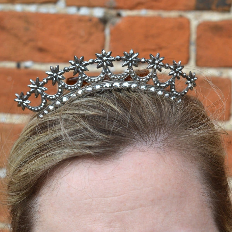 Tiara aus georgianischem Stahl mit Sternmotiv im Haar vor einem rustikalen Backsteinhintergrund.