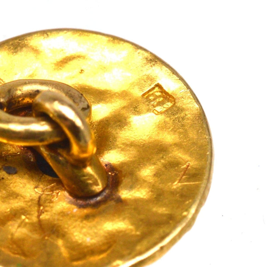 Nahaufnahme eines texturierten goldenen Manschettenknopfes mit Punzierung und Kettenglieddetail.