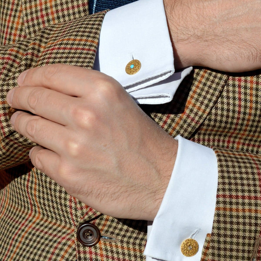 Nahaufnahme eines Mannes mit goldenen Manschettenknöpfen mit Türkis aus den 1960er Jahren, ergänzt durch einen stilvollen karierten Blazer.