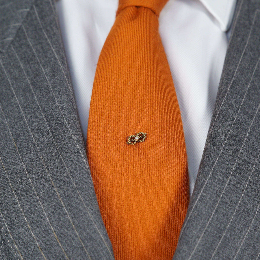 Edwardian 15ct gold lovers knot tie pin with natural pearl on an orange tie, circa 1900s.