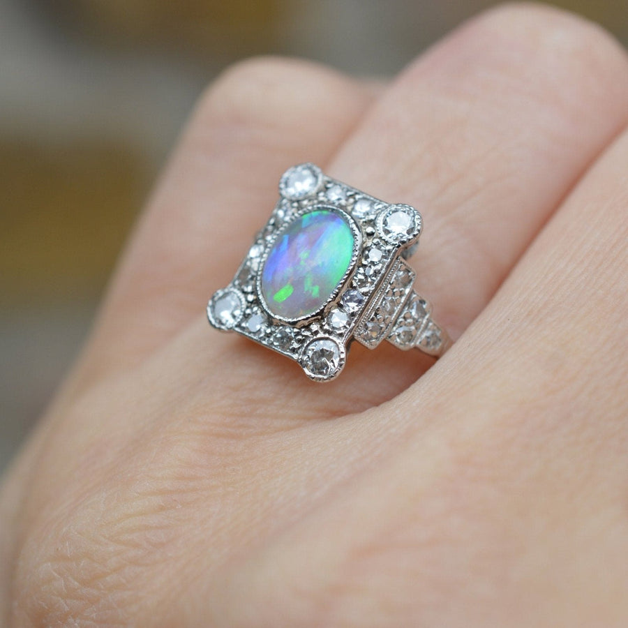 Art-Déco-Ring aus 18 Karat Gold und Platin mit einem ovalen Opal, der von zehn Diamanten umgeben ist, und einem eleganten, detaillierten Design.