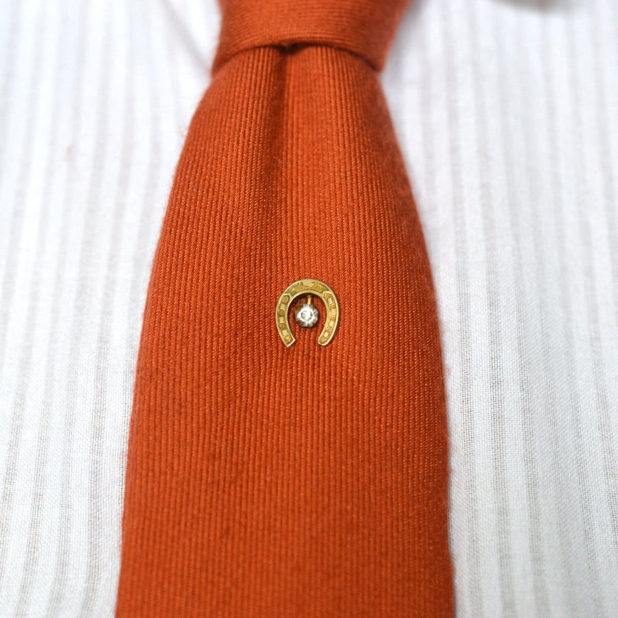 Art Deco Hufeisen Krawattennadel mit klarer Paste auf einer orangefarbenen Krawatte, symbolisiert Glück und Schutz.