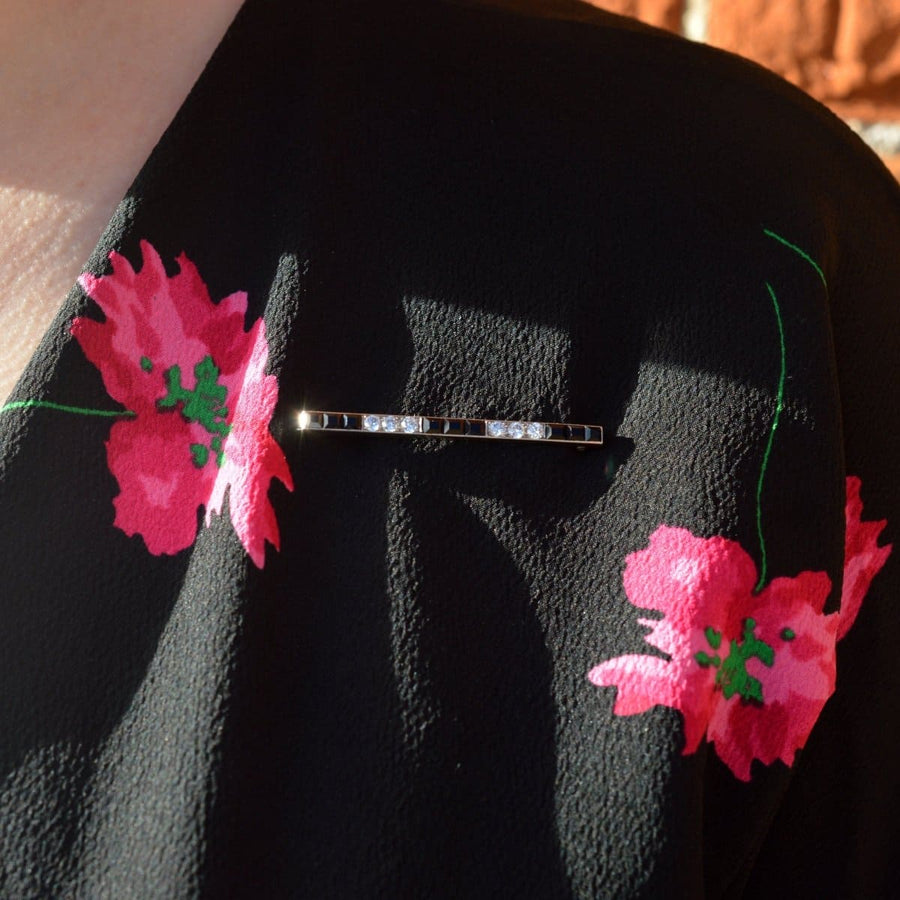 Art-Deco-Brosche aus Platin mit Onyx und Diamanten am Revers eines Blumenkleides.