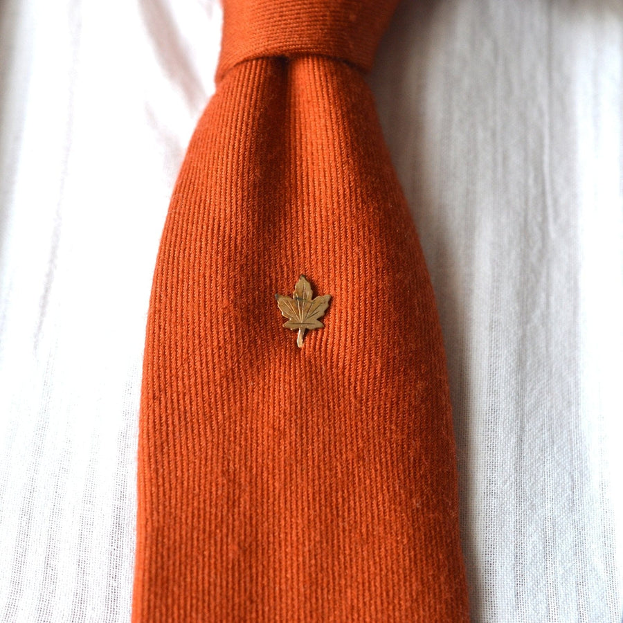 Art Deco Krawattennadel aus gerolltem Goldblech mit Ahornblatt auf einer orangefarbenen Krawatte, die Kanada und die keltische Mythologie symbolisiert.