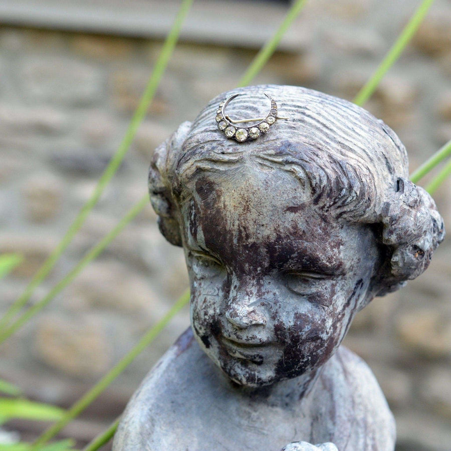 Silver crescent moon paste brooch on a vintage statue, symbolizing new beginnings and timeless elegance.