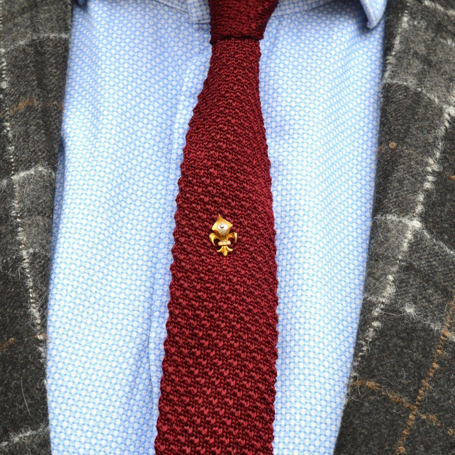 Edwardianische Fleur de lys Krawattennadel aus 18 Karat Gold auf einer strukturierten weinroten Krawatte, die stilvoll mit einem gemusterten Blazer kombiniert wird.