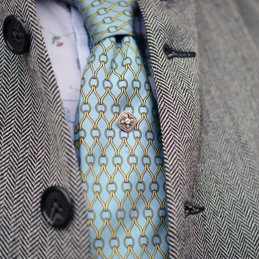 Elegante blau gemusterte Krawatte mit metallischer Krawattennadel, ergänzt durch eine Fischgrätjacke.