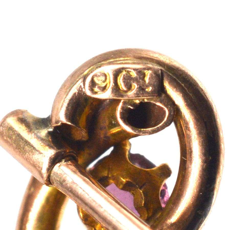 Nahaufnahme der Edwardian 9ct gold lover's knot Krawattennadel zeigt Punzen und lebendige Granat Detail.