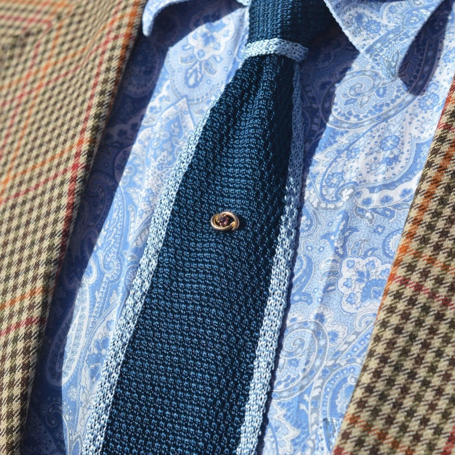 Edwardian 9ct gold lover's knot Krawattennadel mit Granat auf einer blauen Krawatte, gestylt mit einem karierten Blazer.