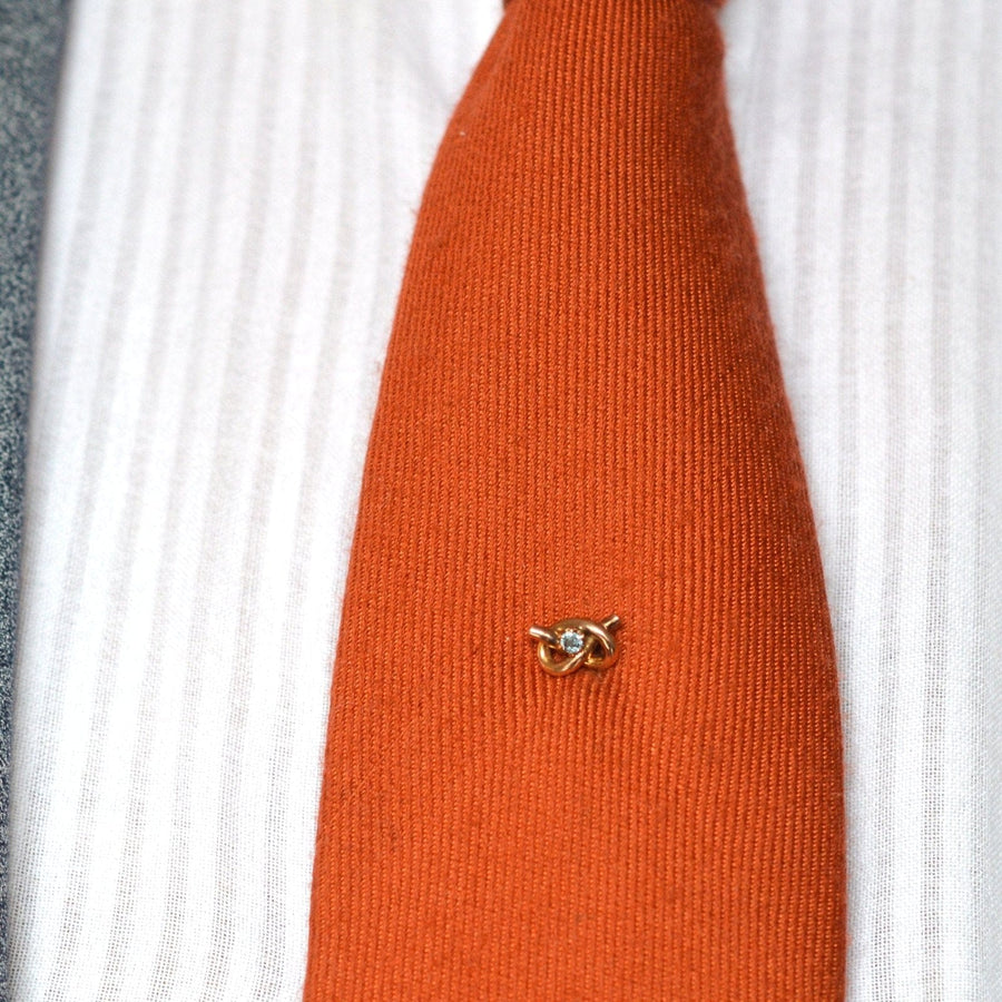 Krawattennadel mit Liebesknoten aus 9 Karat Gold mit Aquamarin auf einer orangefarbenen Seidenkrawatte, die die Eleganz der Edwardianischen Ära zeigt.