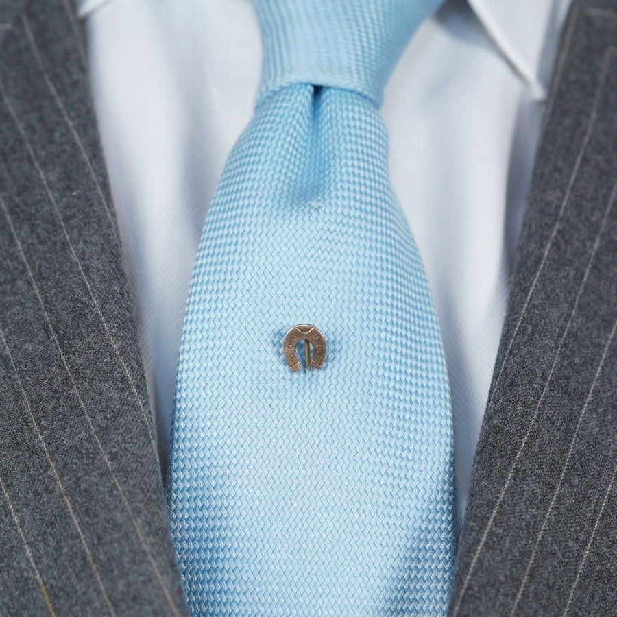 Krawattennadel aus 9 Karat Gold mit Glückshufeisen, getragen auf einer hellblauen Krawatte zu einem grauen Anzug.