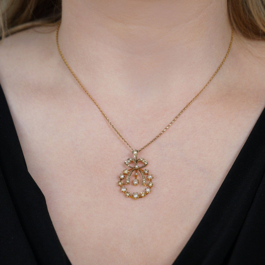 Edwardianischer Anhänger aus 9-karätigem Gold mit gespaltenen Perlen und Schleifenmotiv, am Hals eines Modells.