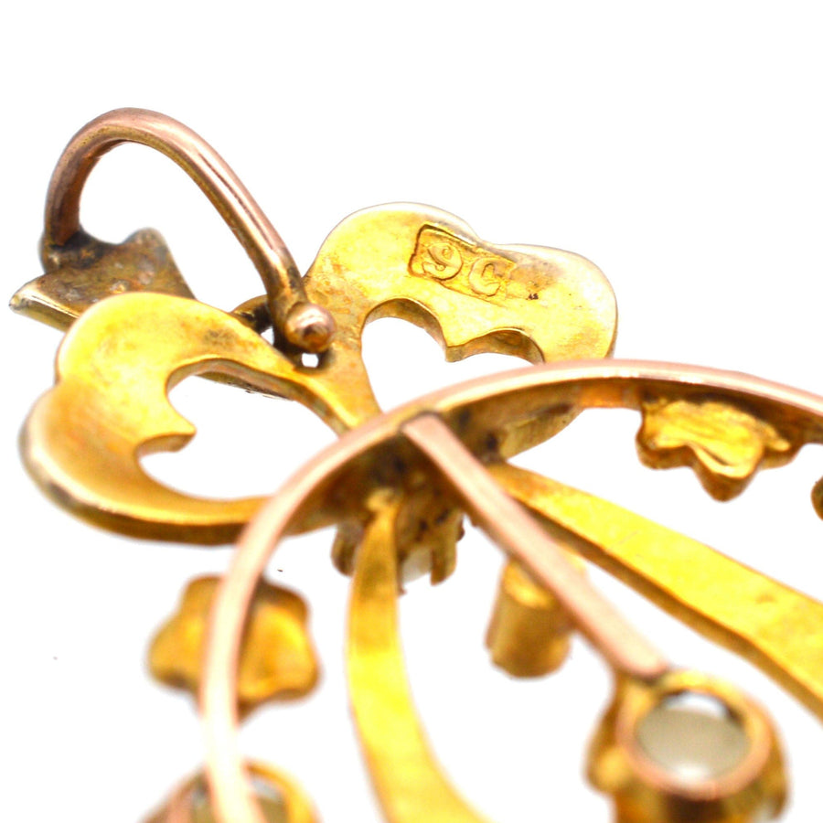 Nahaufnahme eines edwardianischen Anhängers aus 9-karätigem Gold mit zartem Schleifenmotiv und geteilten Perlen, die komplizierte Details hervorheben.