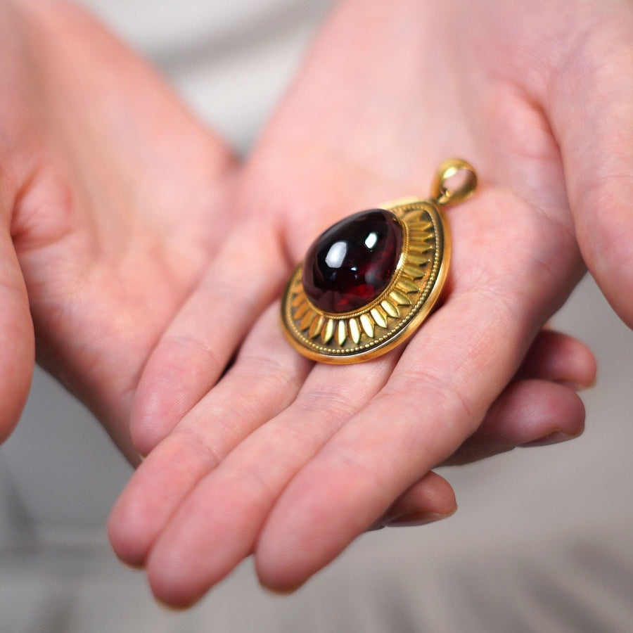 Großer viktorianischer Cabochon-Granat-Anhänger aus 15 Karat Gold, der in den Händen gehalten wird und aufwändige Golddetails aufweist.