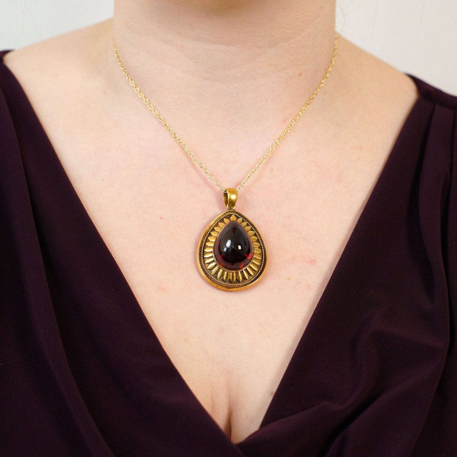 Großer Goldanhänger mit einem Cabochon-Granat, der am Hals eines Models getragen wird und den Stil des antiken Schmucks zeigt.
