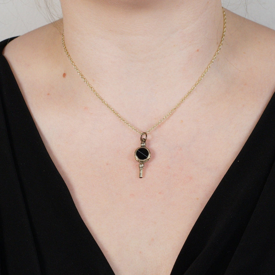 Schlüsselanhänger mit Goldgehäuse und Onyxband an einer zarten Kette, die antike Eleganz ausstrahlt.