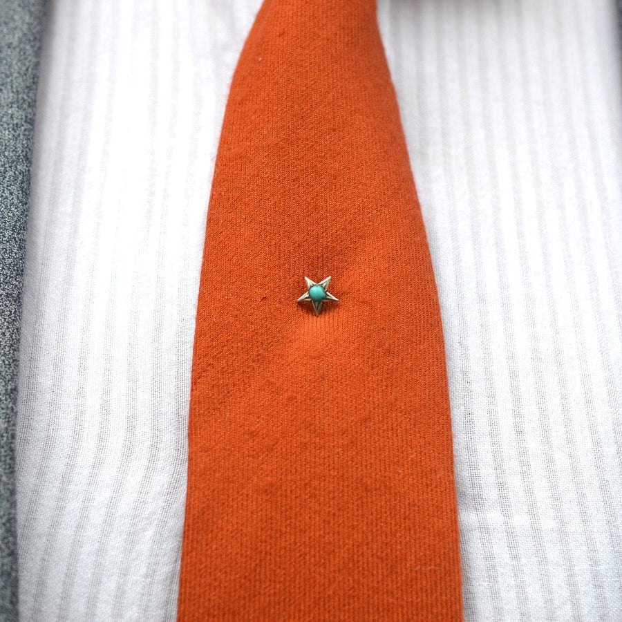 Viktorianische Krawattennadel mit silbernen und türkisfarbenen Sternen, die eine orangefarbene Krawatte akzentuiert und Liebe und Erinnerung symbolisiert.