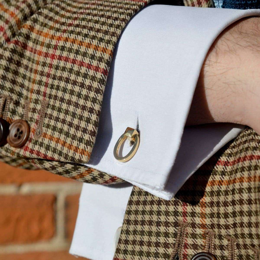 Nahaufnahme von Manschettenknöpfen aus 18-karätigem Gold an einem weißen Hemd und einem gemusterten Blazer.