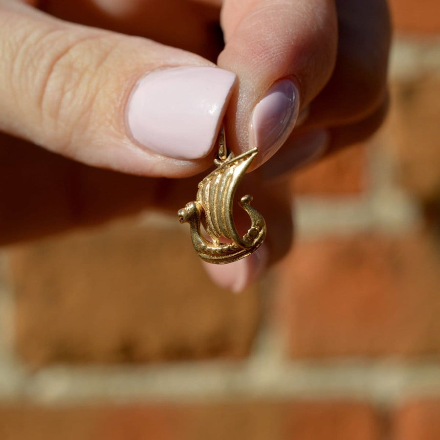 In der Hand hält er einen Wikingerschiff-Charm aus 9 Karat Gold, der seinen Drachenkopf vor einem Hintergrund aus Ziegelsteinen zur Schau stellt.