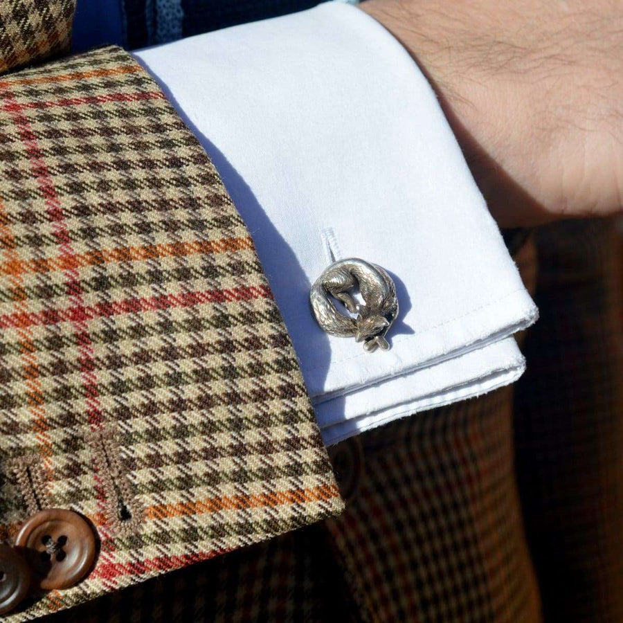 Silberne Manschettenknöpfe mit schlafendem Fuchs, getragen zu einem weißen Hemd und einem Blazer mit Hahnentrittmuster.