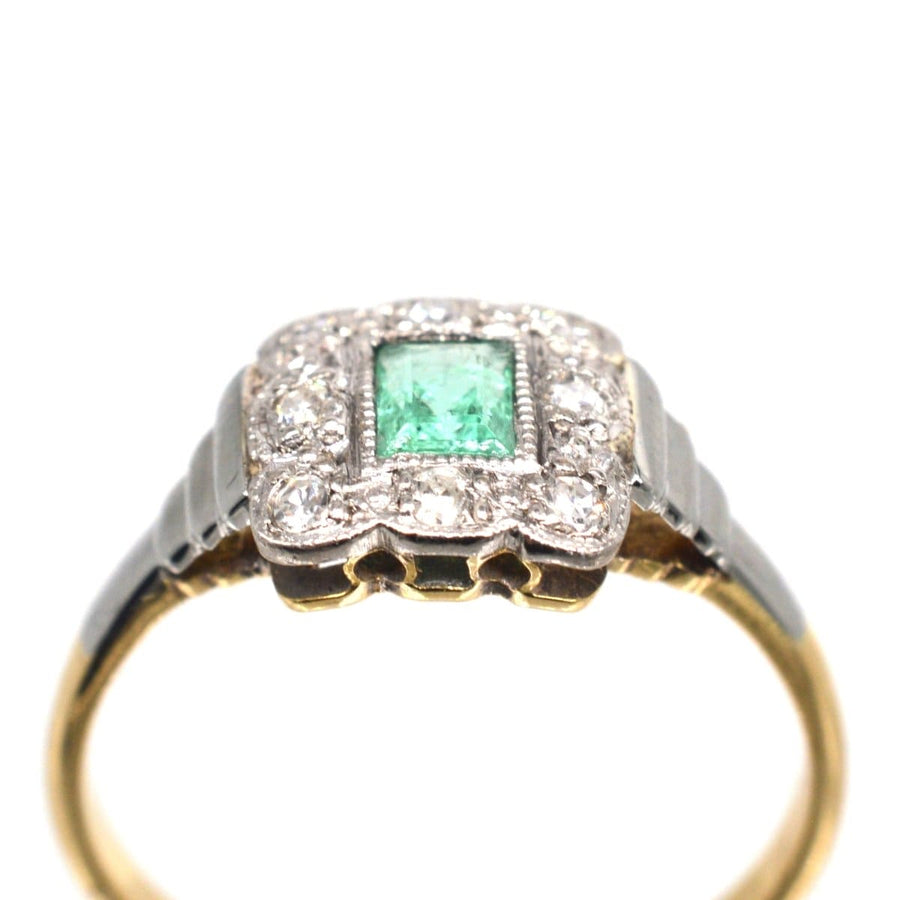 Art Deco 18ct gold and platinum ring featuring an emerald surrounded by diamonds in a classic millegrain setting.