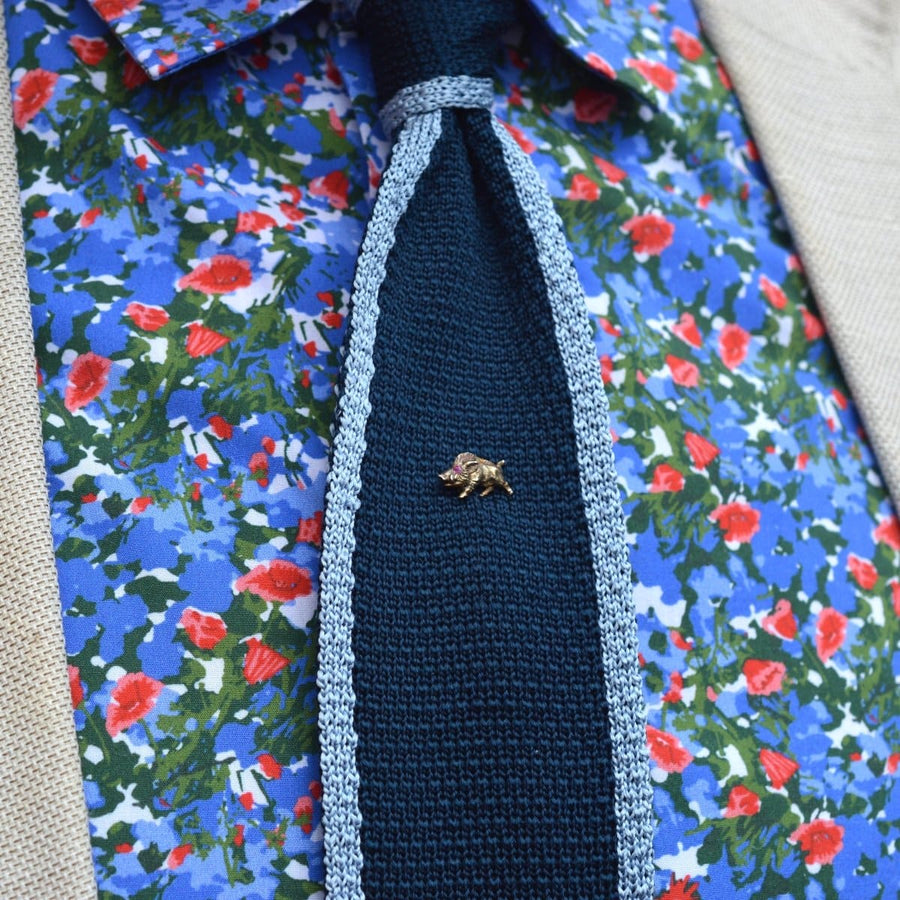 Edwardian 14ct gold wild boar tie pin with ruby eyes on a dark tie, set against a colorful floral shirt.