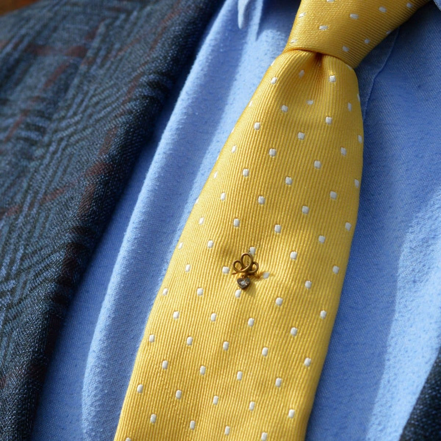 Edwardian 15ct gold knot tie pin with a dangling diamond heart on a yellow tie, symbolizing timeless love.