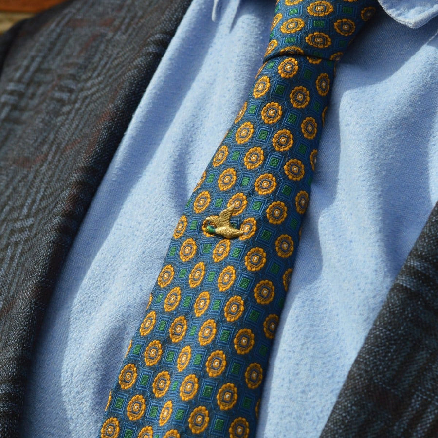 Elegant tie featuring a vibrant blue and gold pattern, secured with an Edwardian gold and enamel duck tie pin.