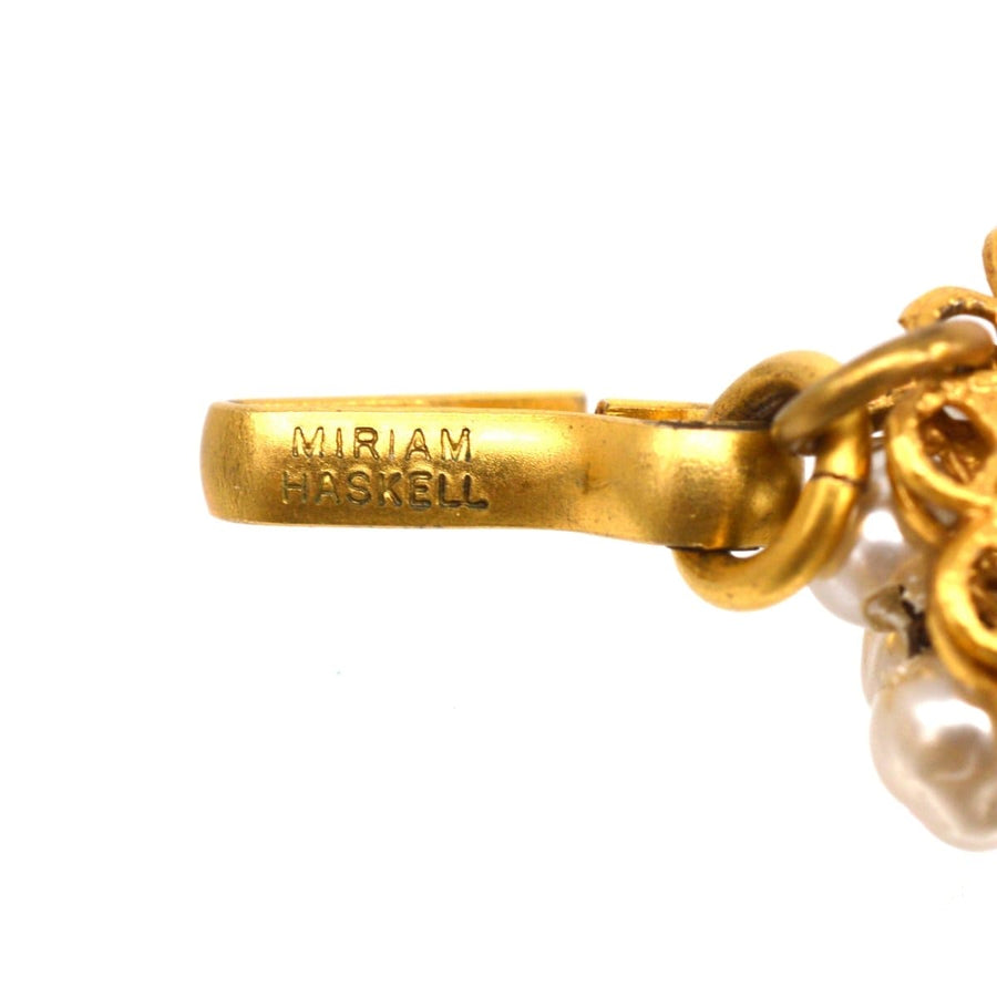 Close-up of Miriam Haskell signed gold-tone clasp on faux pearl floral necklace, showcasing intricate design.