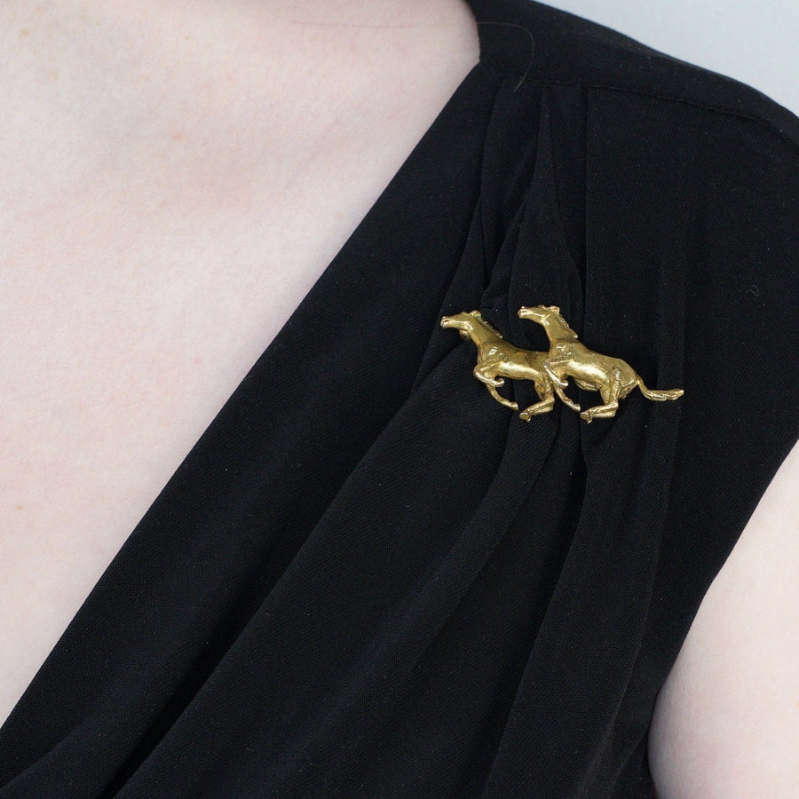 1940s 9ct gold galloping horses brooch on black dress by Alabaster & Wilson, symbolizing companionship.