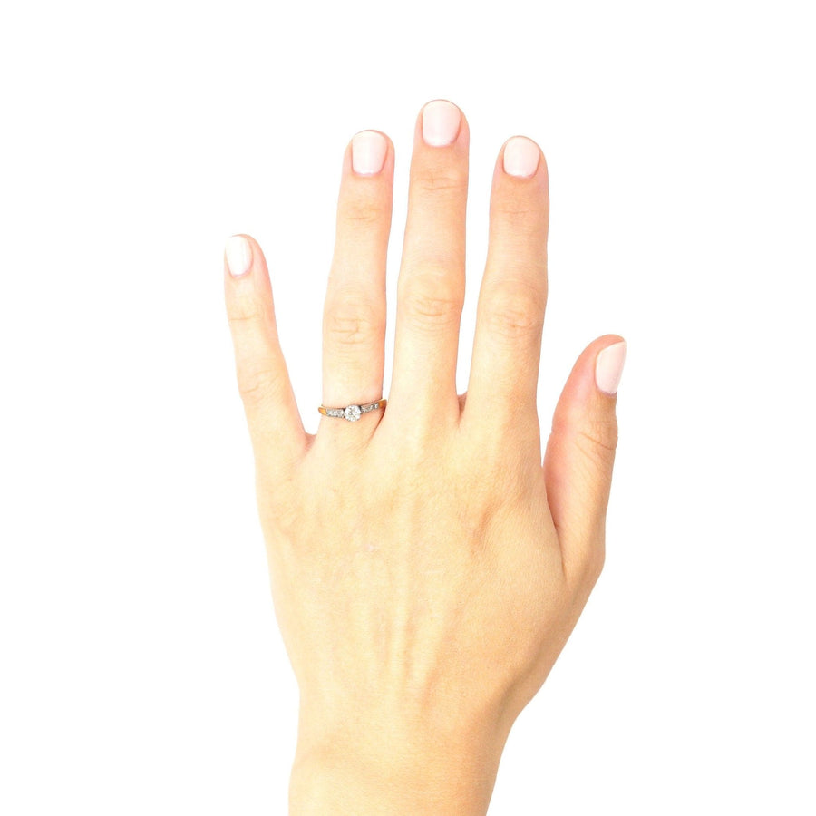 Art Deco 18ct gold and platinum diamond solitaire ring with diamond shoulders on a hand.