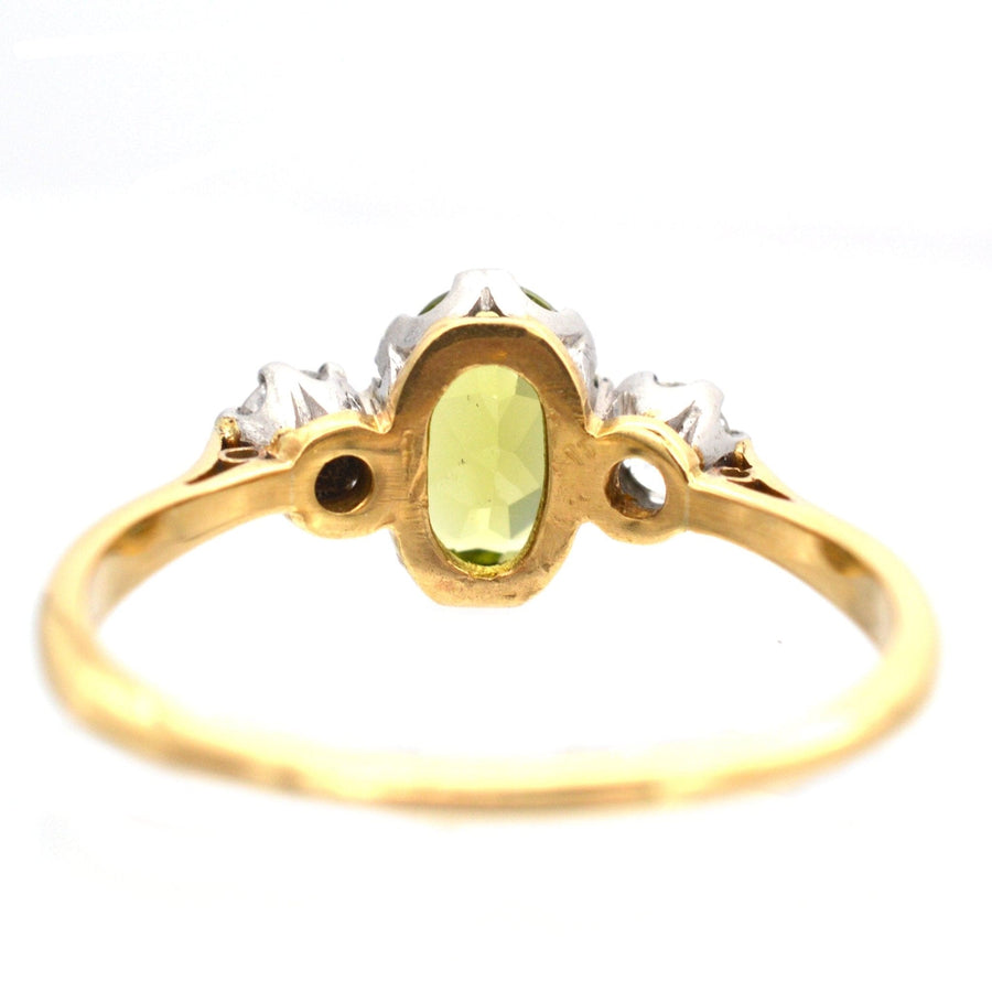 Art Deco three stone ring featuring a central peridot and diamond accents set in 18ct gold and platinum.