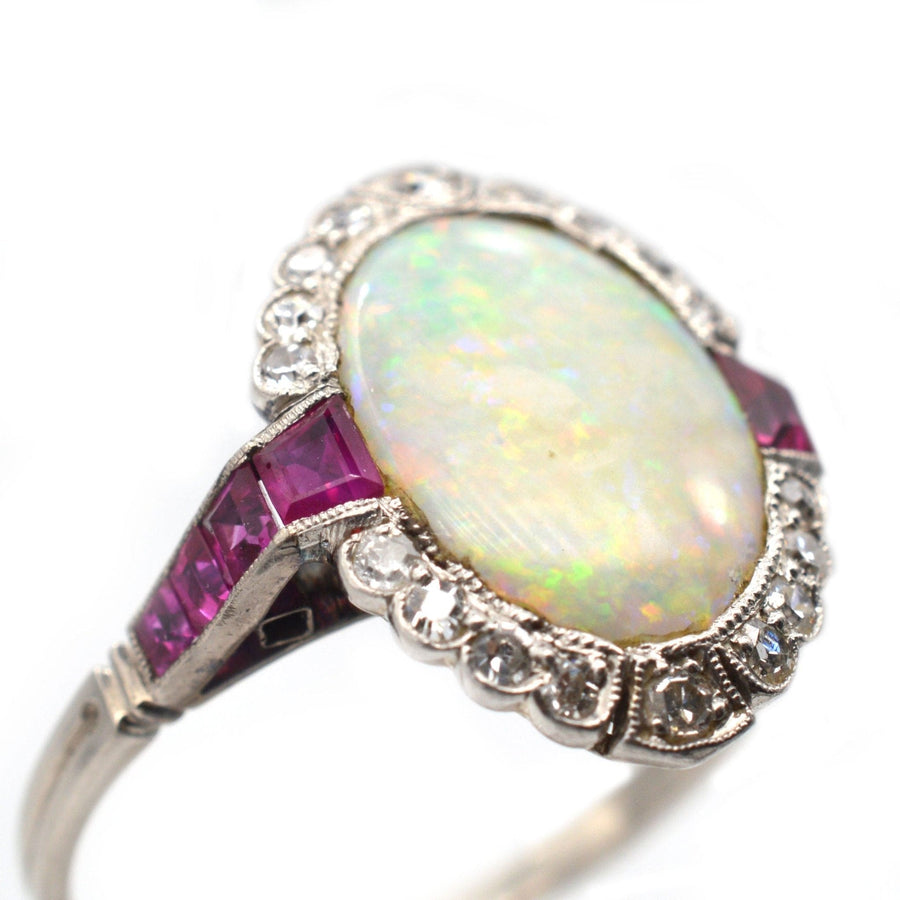 Art Deco 18ct white gold ring featuring an oval opal, Burma rubies, and diamond accents, showcasing vibrant color play.