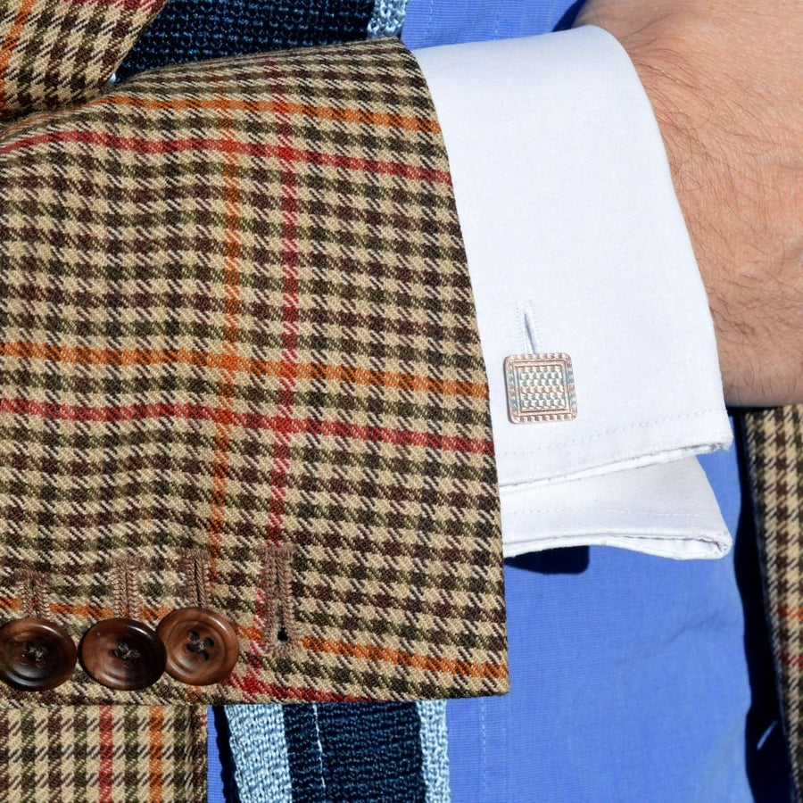 Close-up of a stylish cuff with Art Deco two-color gold cufflinks on a patterned jacket sleeve.
