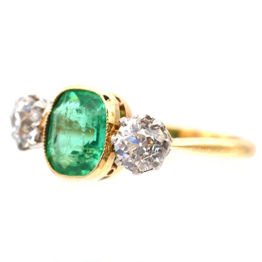 Art Deco three stone ring featuring a vibrant emerald flanked by diamond accents set in yellow gold.