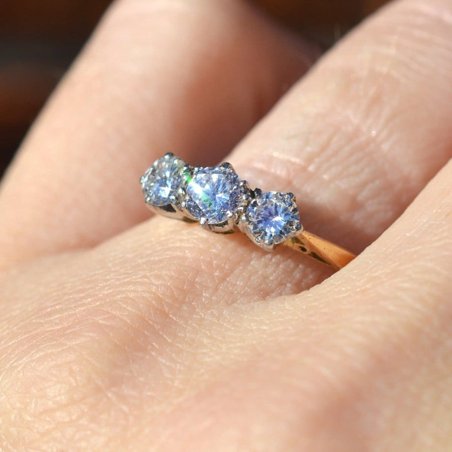 Art Deco platinum and 18ct gold three stone diamond ring worn on a finger, showcasing large bright diamonds.