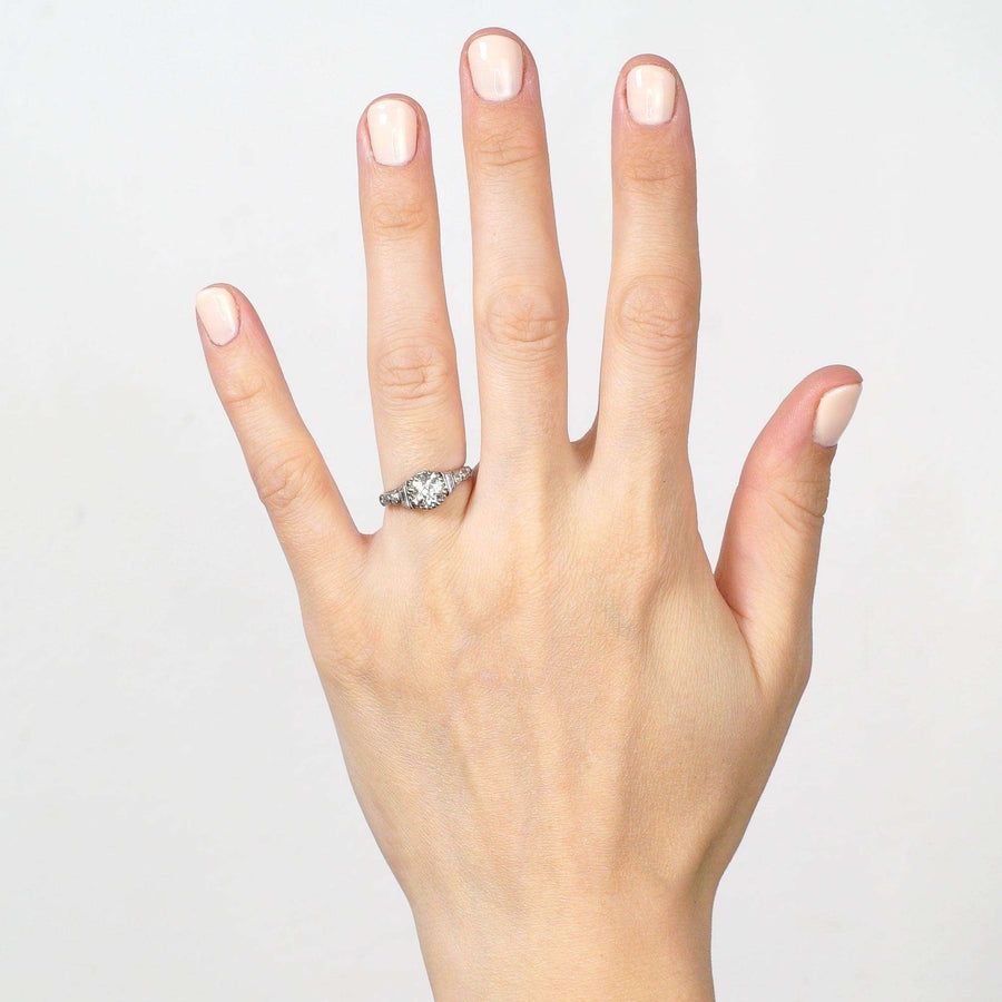 Art Deco platinum large diamond solitaire ring with diamond shoulders worn on a hand.