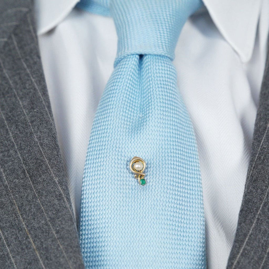 Art Nouveau gold tie pin with pearl and emerald, worn on a blue tie, adds elegance to formal attire.